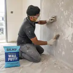 Professional worker cleaning loose material from a wall before applying Silky Wall Putty.