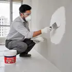 Worker applying Acrylic Wall Putty paste to a wall using a trowel.
